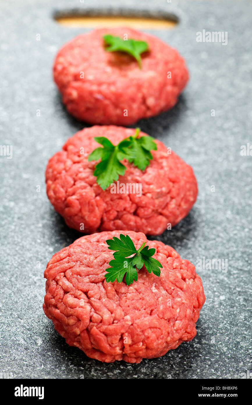 Three ground beef hamburger patties on cutting board Stock Photo
