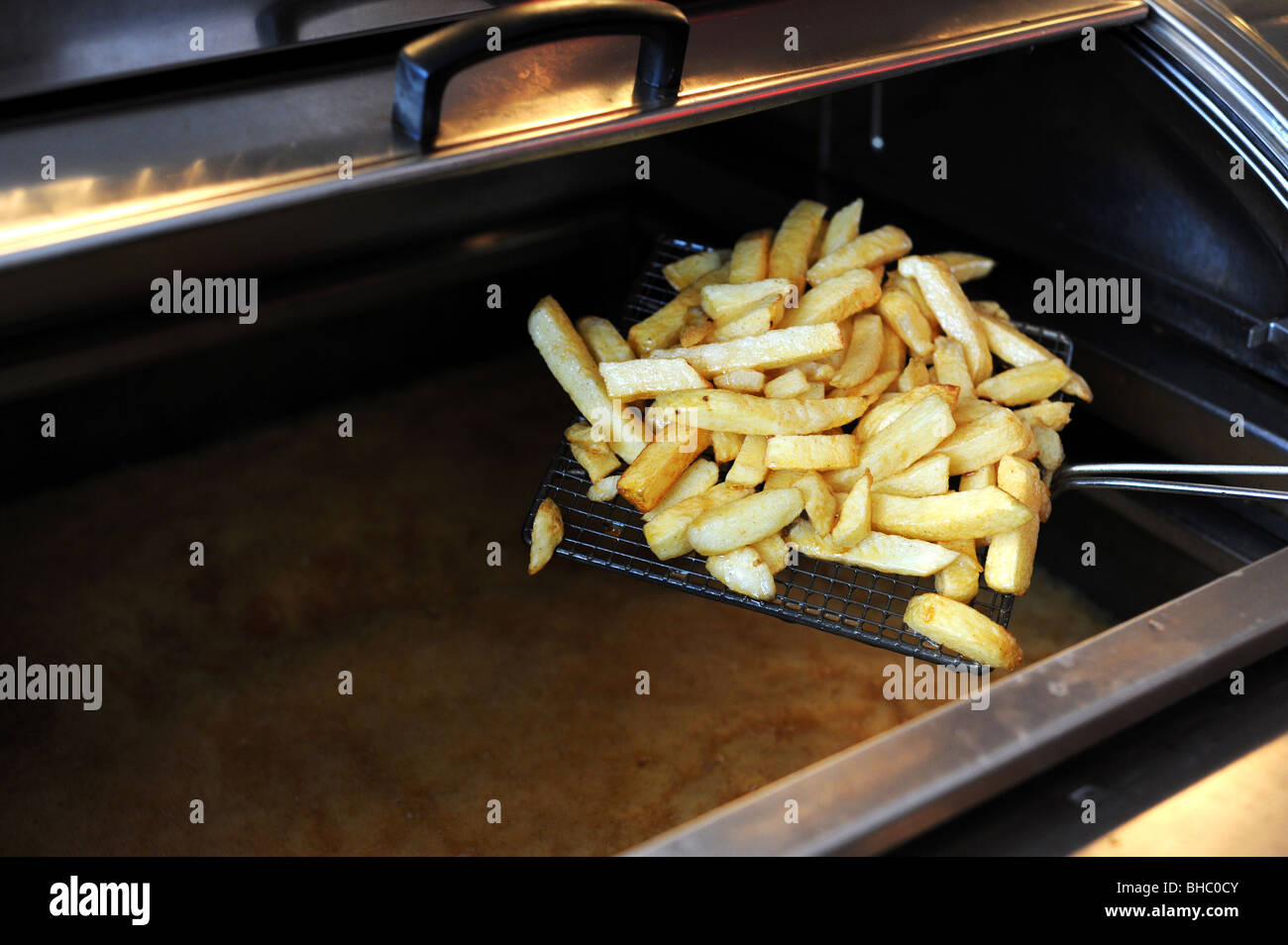 Chips come out of the deep fat fryer in fish and chip shop Stock Photo