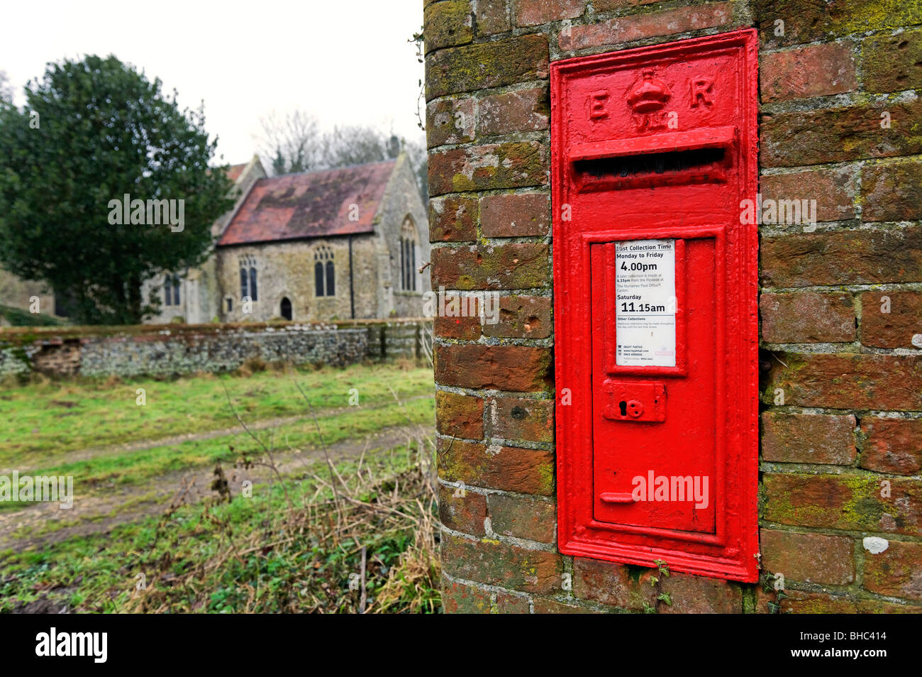 Red post box outside quaint churchyard in rural English village Norfolk UK Stock Photo