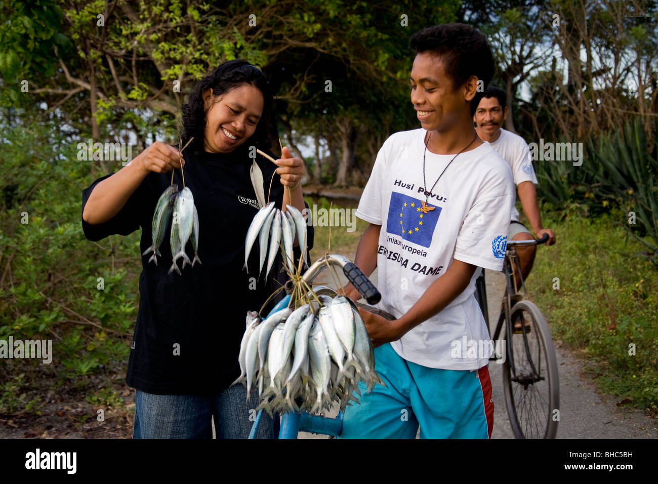Woman  buying fresh fish from young fisherman selling fish from bike on a track to  Suai-Loro East Timor Stock Photo