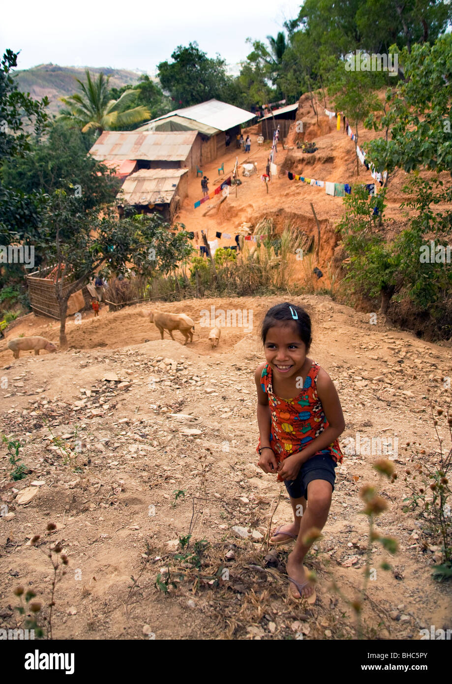 Young girl on hillside above remote mountain village of shacks where poor farmers rearing pigs in East Timor Stock Photo
