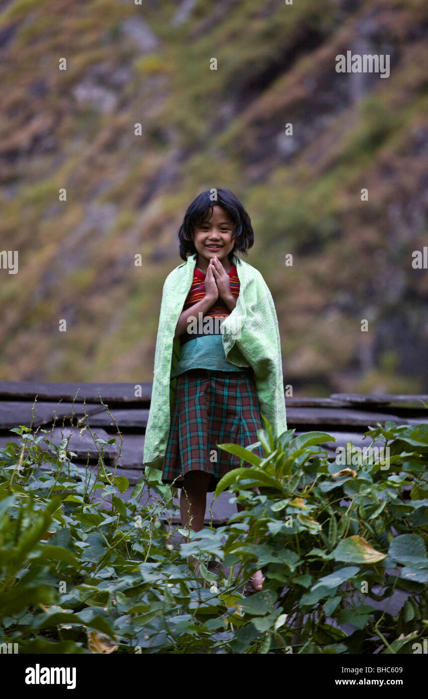 A smiling NEPALI GIRL gives us a NAMASTE on the roof of her village home - AROUND MANASLU TREK, NEPAL Stock Photo