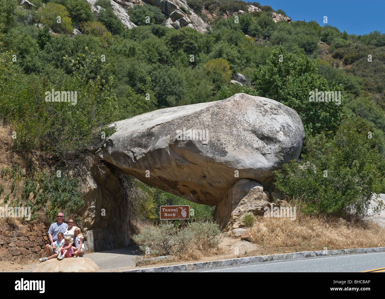Huge boulder fallen from eroded mountain cliff and lying on top of solid rock forming shaped entrance on road going to mountain. Stock Photo