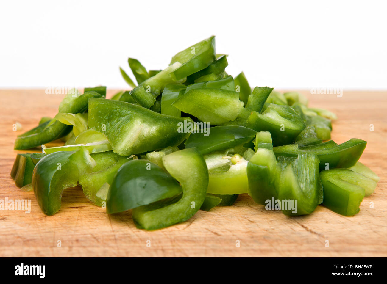 Close up of chopped green peppers on wooden chopping board against a white background Stock Photo