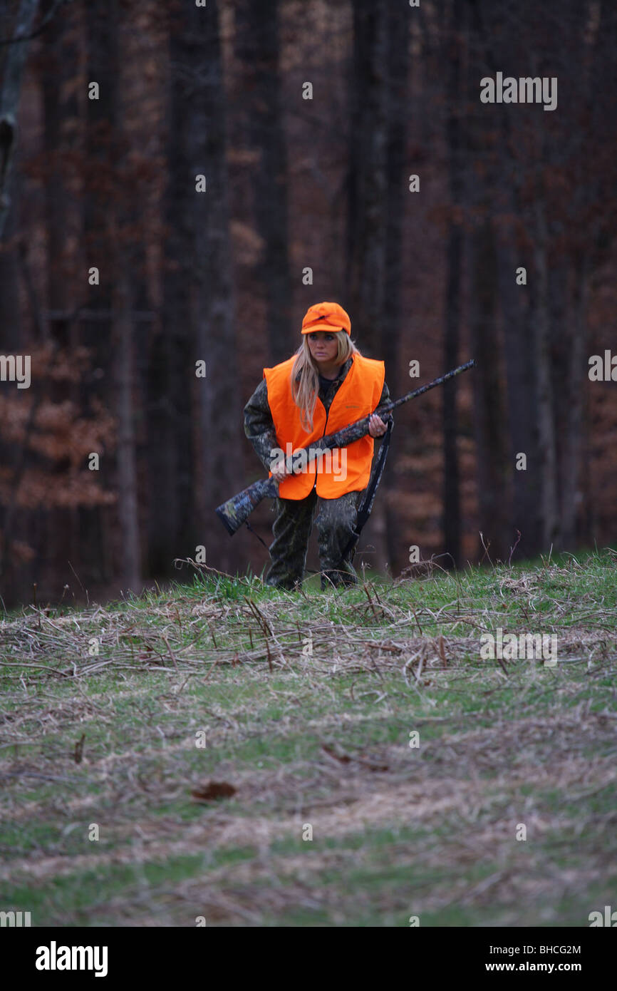 YOUNG WOMAN 21 Y.O. FEMALE HUNTER ORANGE BLAZE VEST STORMY KROMER HAT CARRYING RIFLE DEER HUNTING Stock Photo