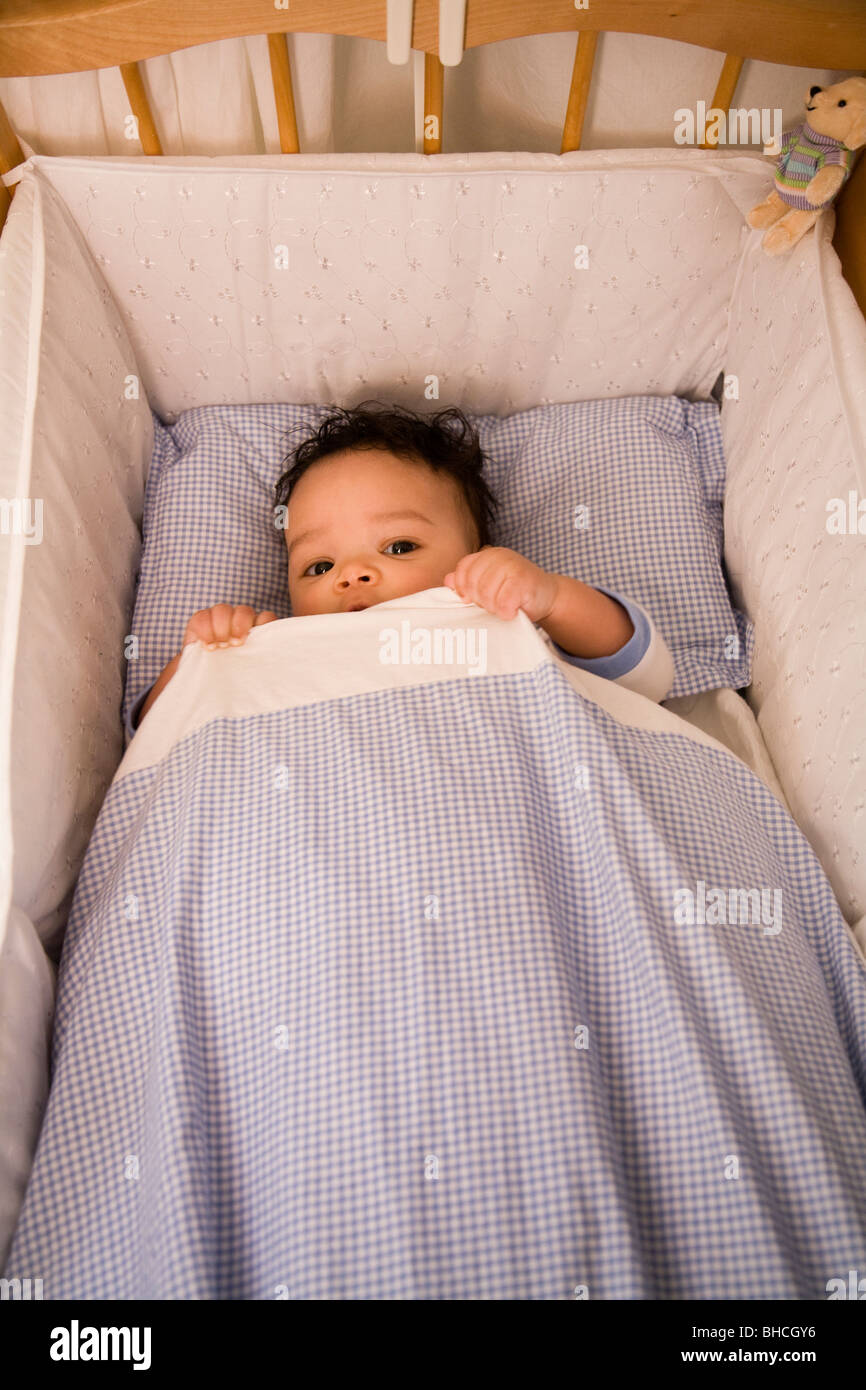 3 1/2 months boy lying in his bed and hiding under his duvet. Stock Photo