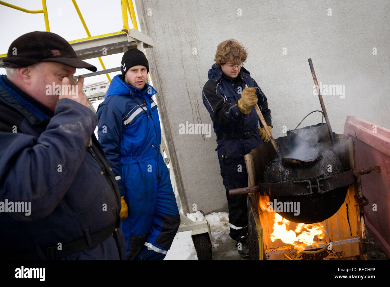 Men working at Vopnafjordur harbour, East Iceland. They are melting tar which is used to seal the concrete joints of the..... Stock Photo