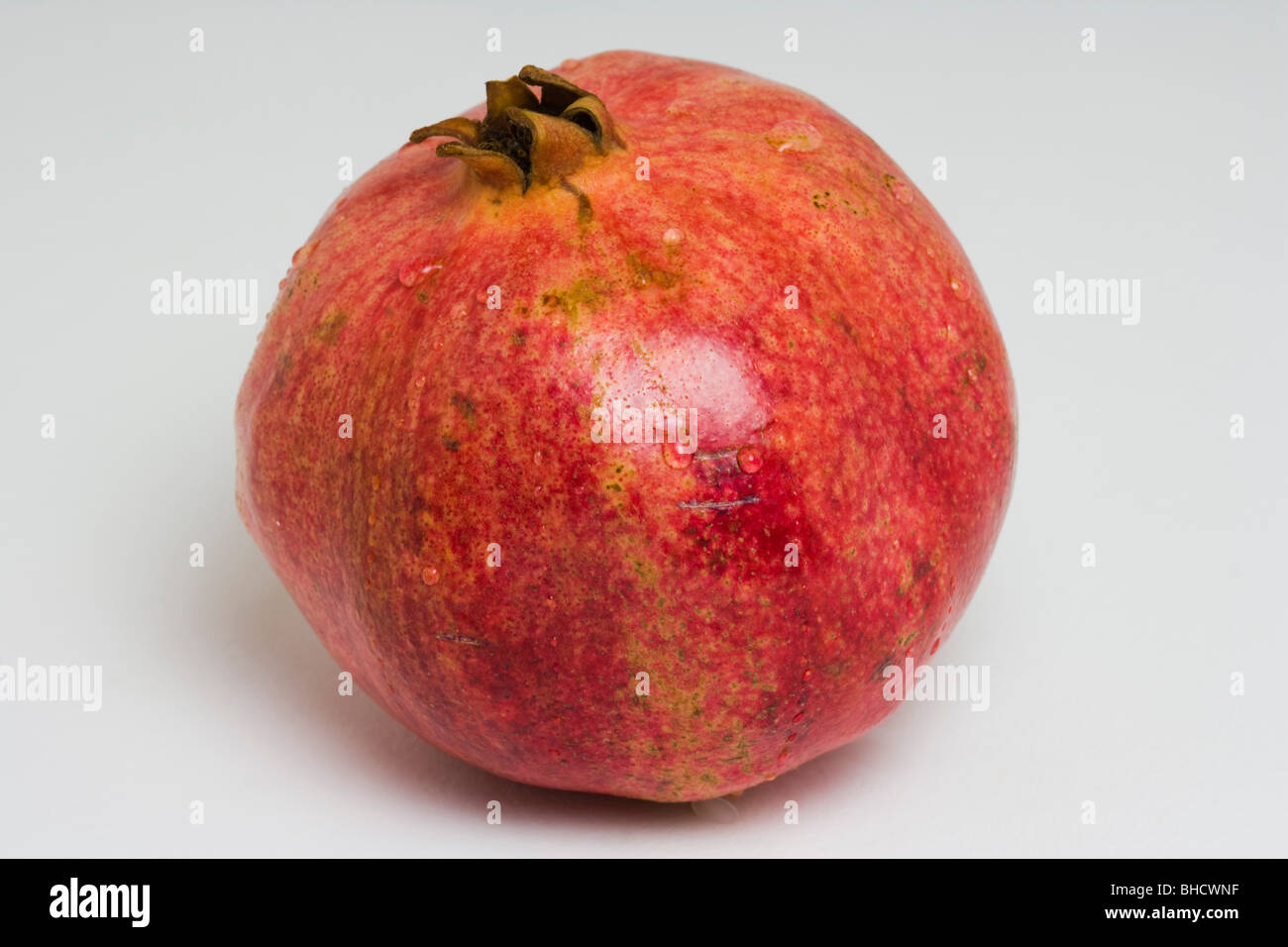 One pomegranate fruit with water drops against white background Stock Photo