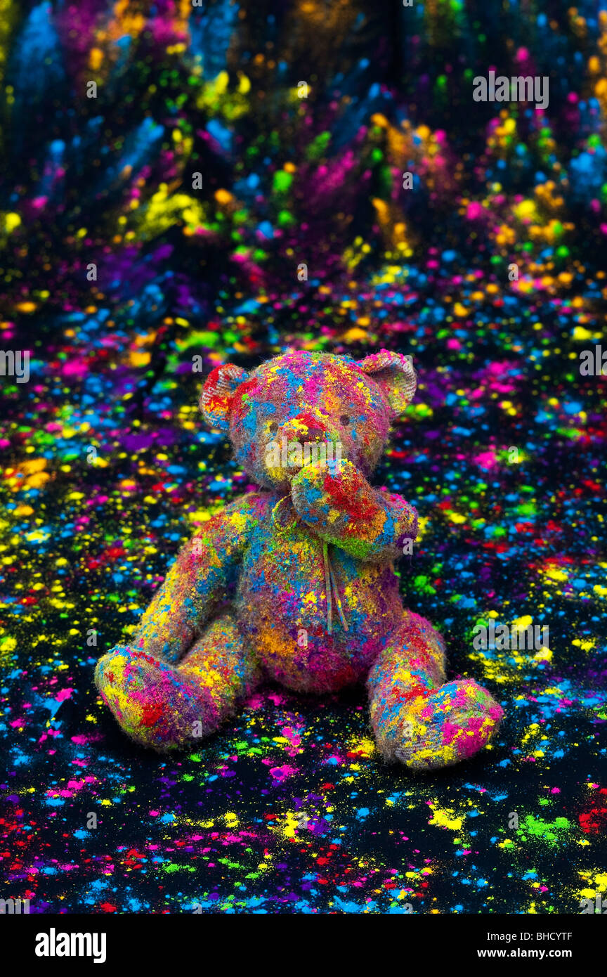 Teddy bear sat on a black cloth covered in coloured powder. Still life Stock Photo