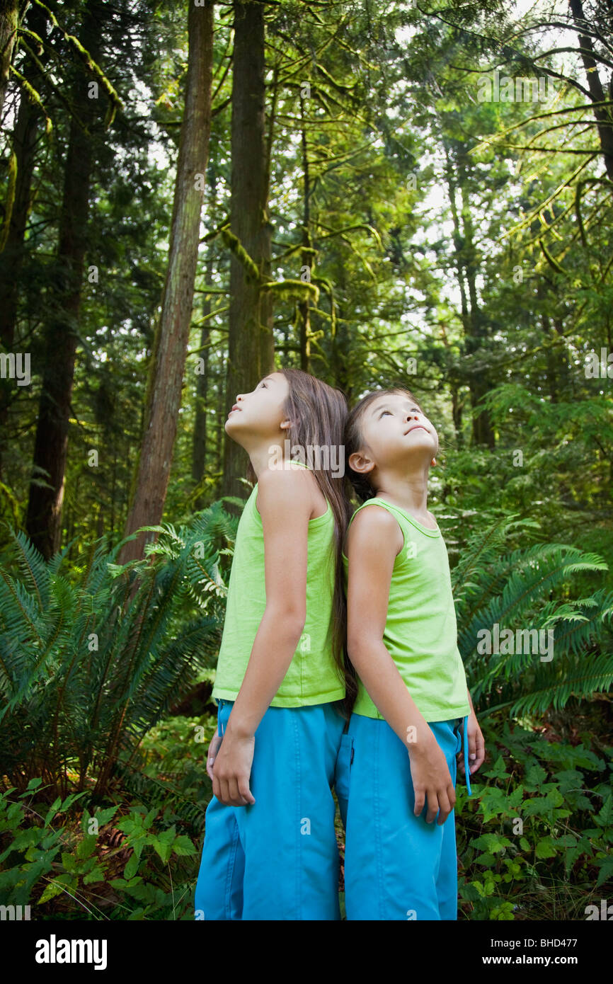 Mixed race girls standing back to back in forest Stock Photo