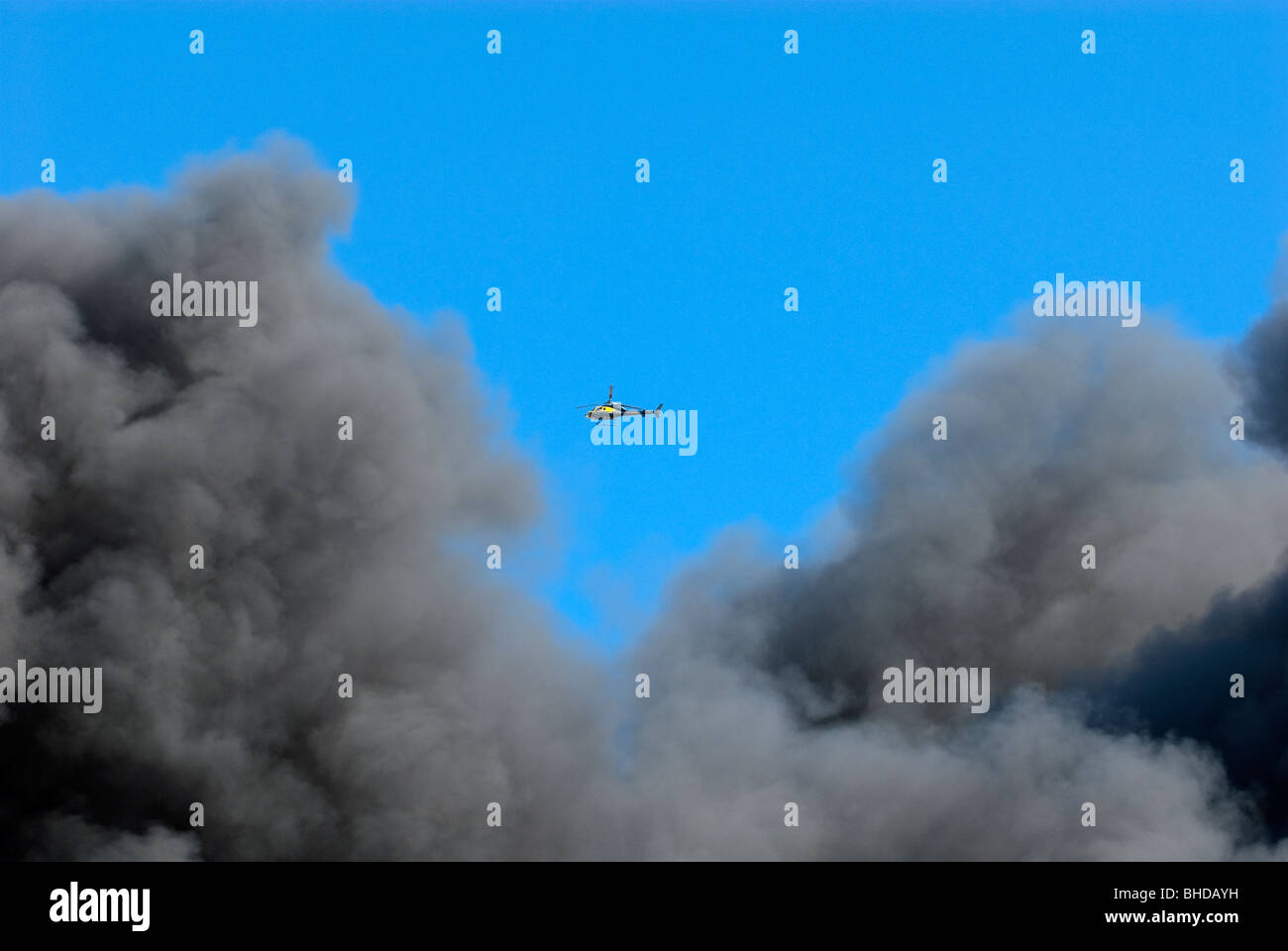 Police helicopter flying into thick black smoke plume at factory fire Stock Photo