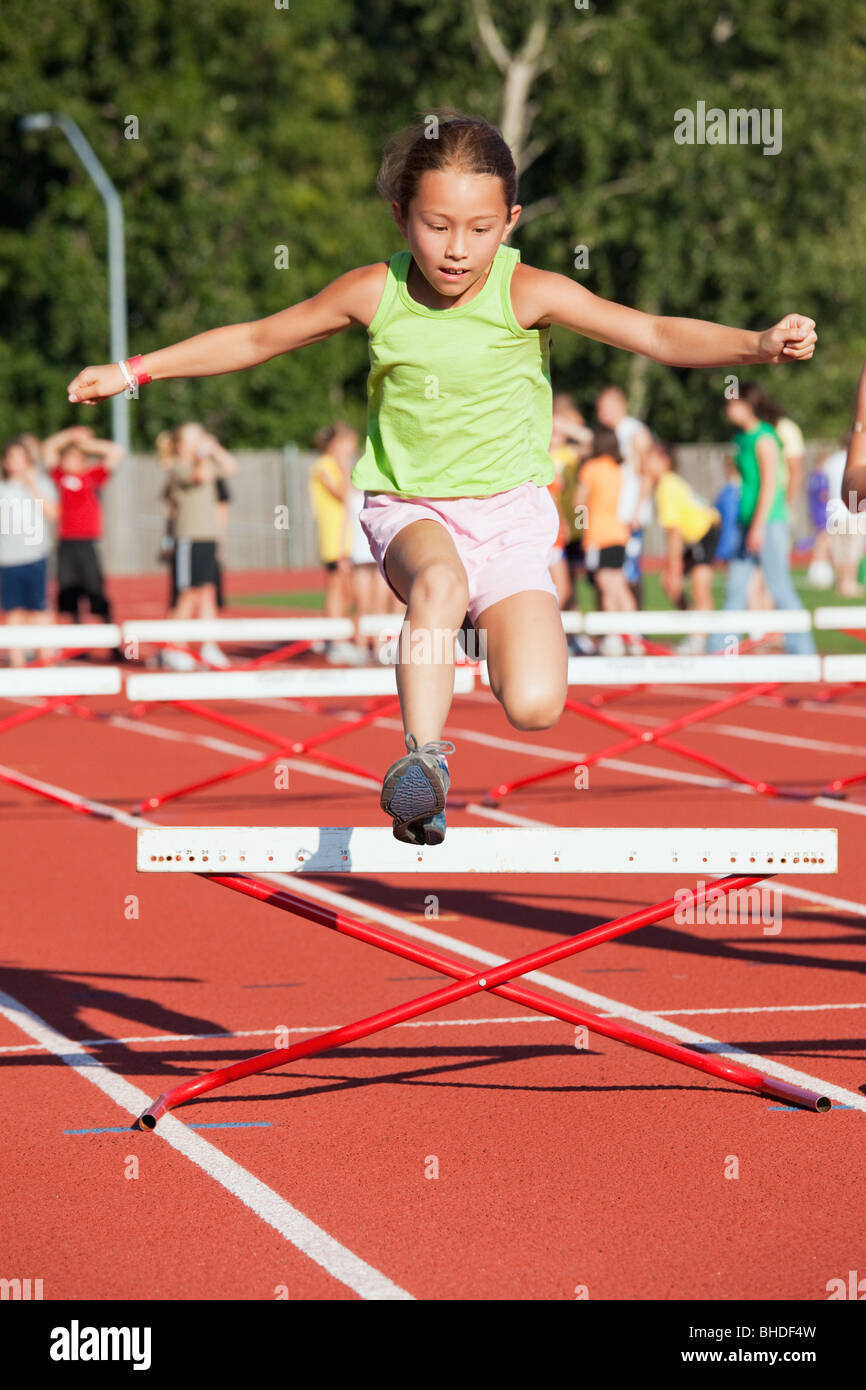 Mixed race girl jumping over hurdle Stock Photo
