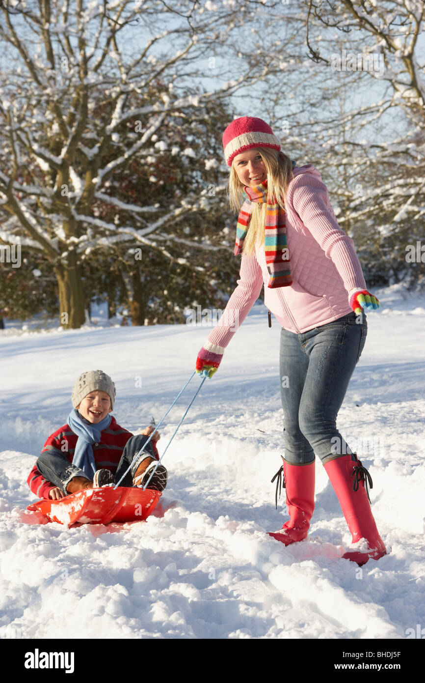 Mother Pulling Son On Sledge Through Snowy Landscape Stock Photo