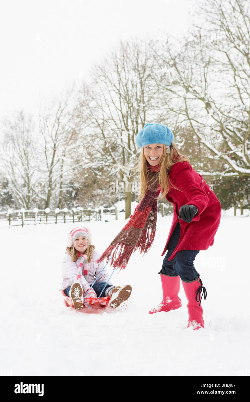 Mother Pulling Daughter On Sledge Through Snowy Landscape Stock Photo