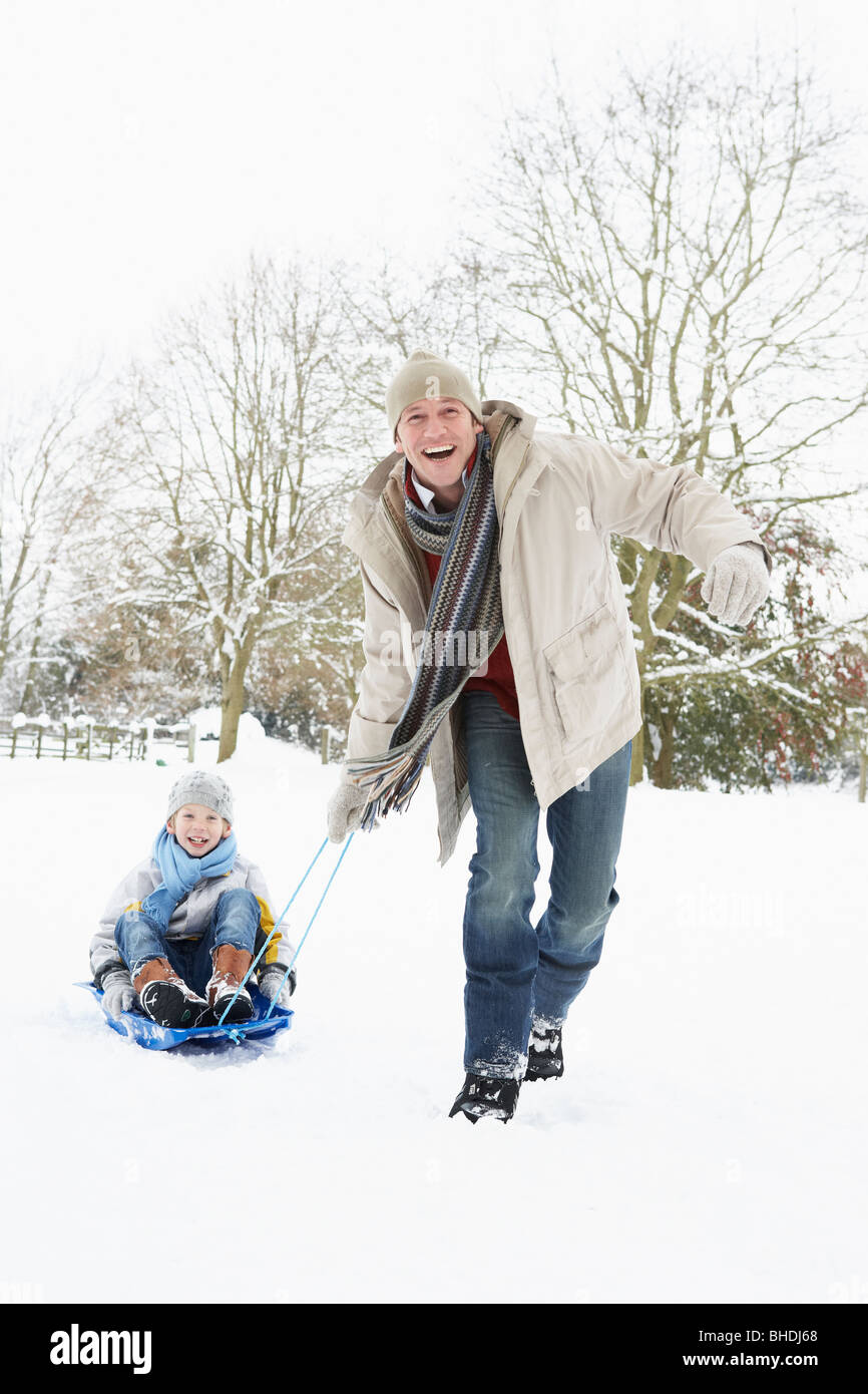Father Pulling Son On Sledge Through Snowy Landscape Stock Photo