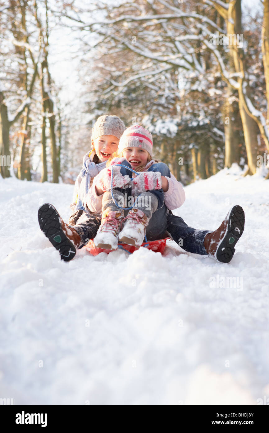 Boy And Girl Sledging Through Snowy Woodland Stock Photo