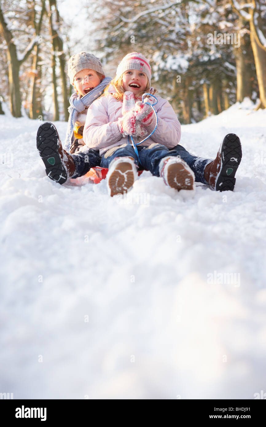 Boy And Girl Sledging Through Snowy Woodland Stock Photo