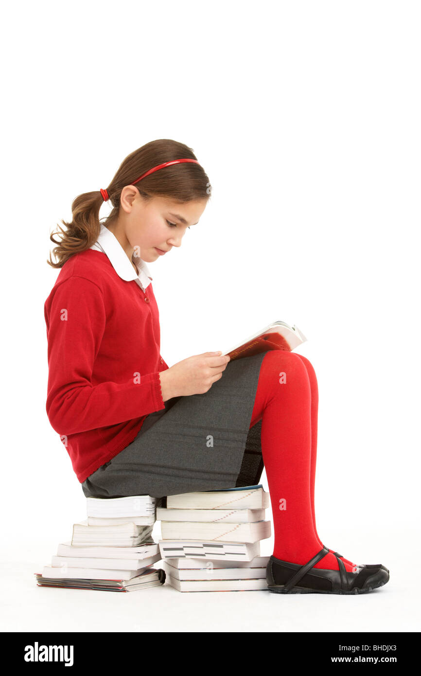 Female Student In Uniform Sitting On Pile Of Books Reading Stock Photo