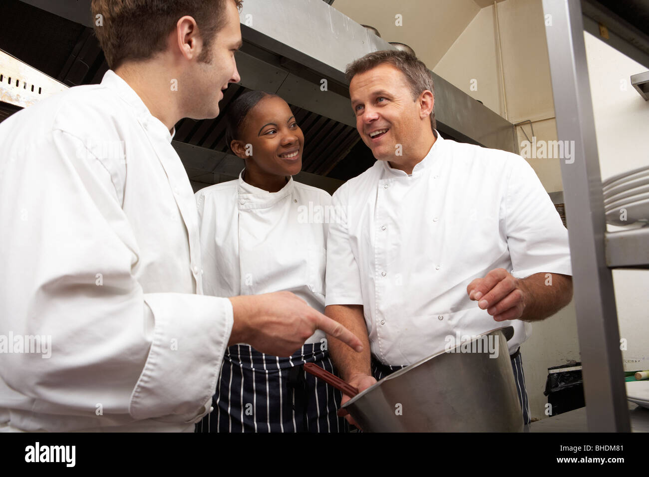 Chef Instructing Trainees In Restaurant Kitchen Stock Photo
