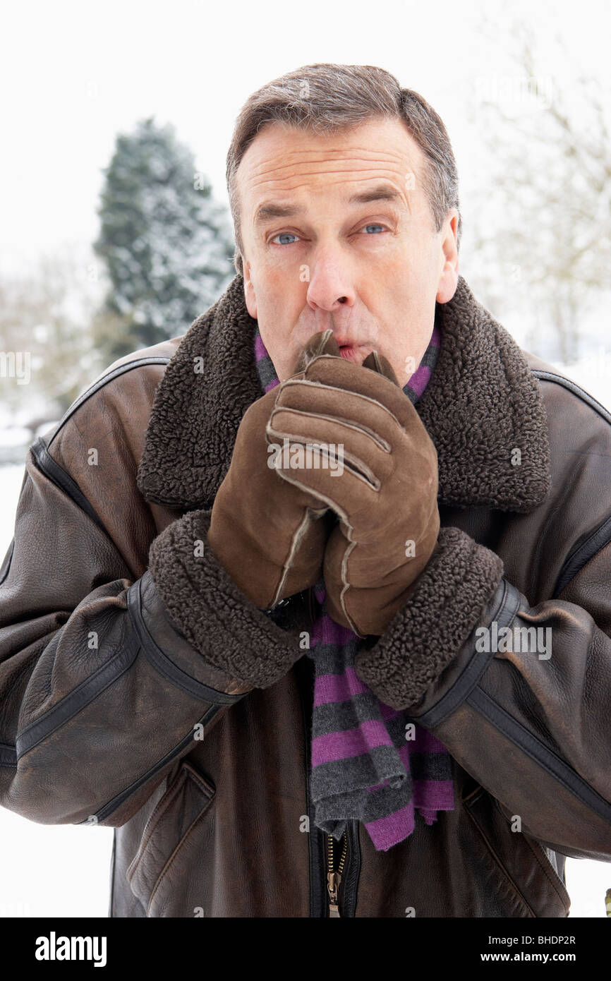 Senior Man Standing Outside In Snowy Landscape Warming Hands Stock Photo