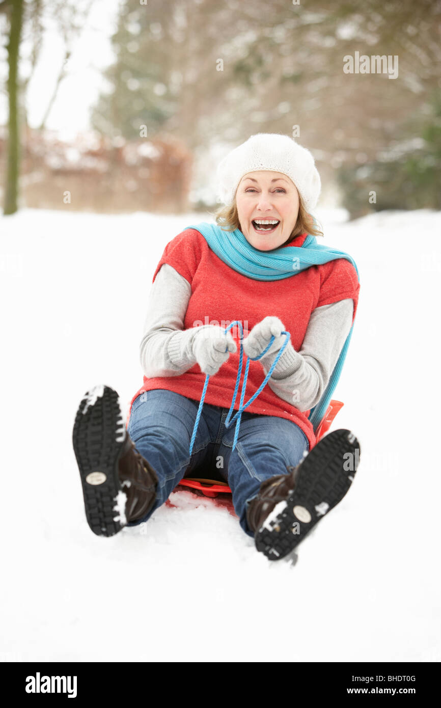 Senior Woman Sledging Through Snowy Woodland Stock Photo