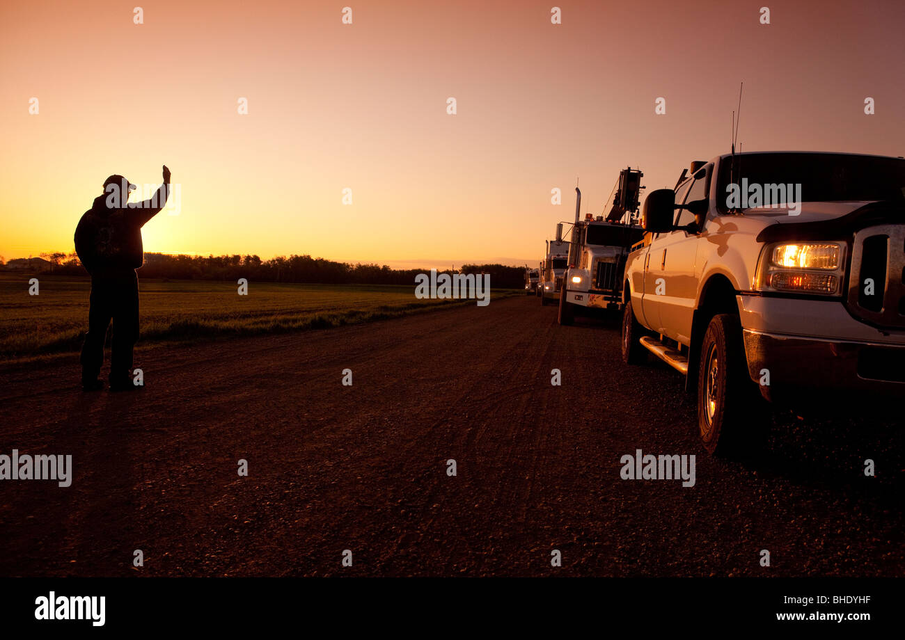 A worker guiding a column of vehicles as they arrive on an oil and gas lease Stock Photo