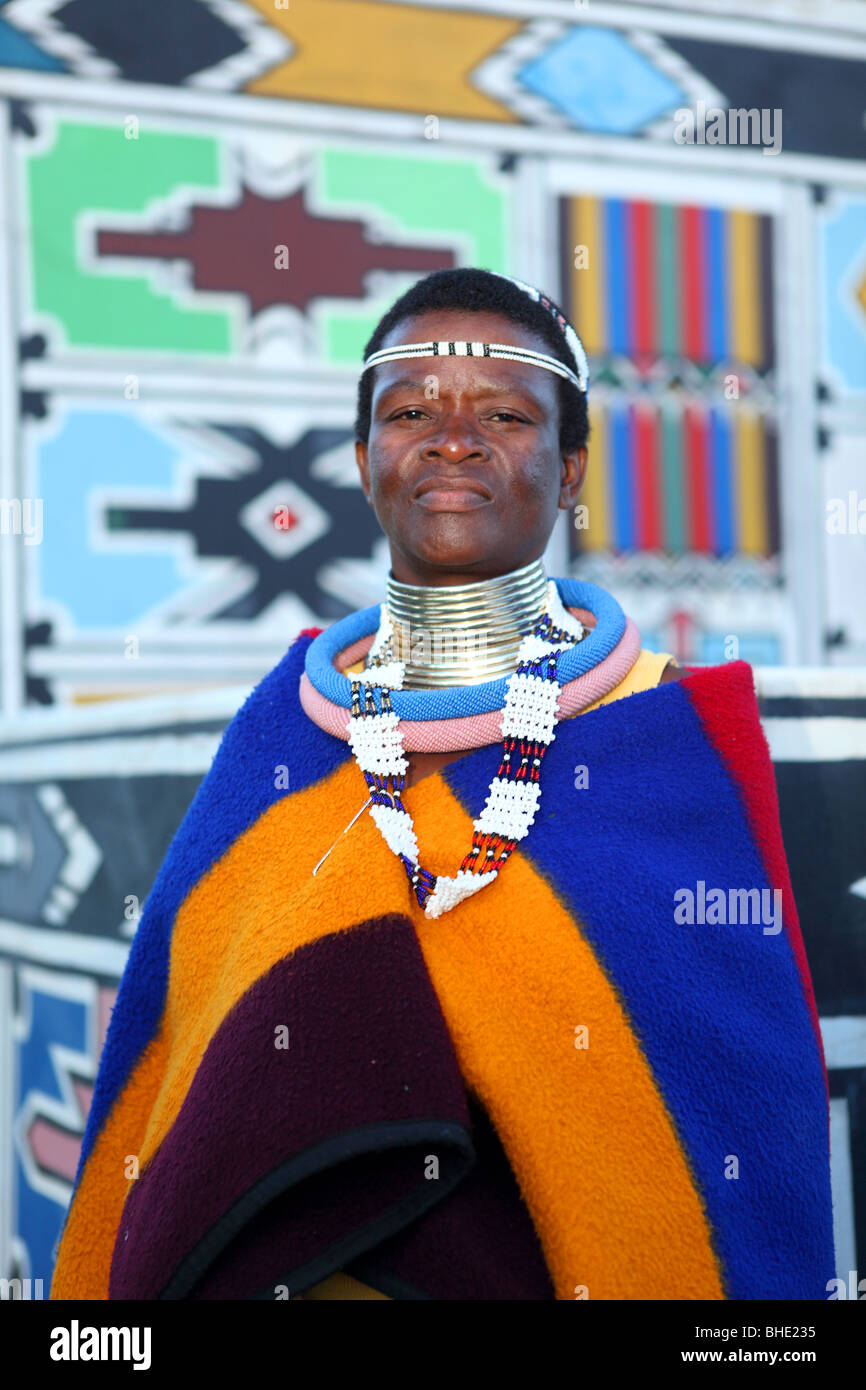 A Ndebele woman in Traditional dress stand in front of a wall decorated in the traditional way at Botshabelo traditional village Stock Photo