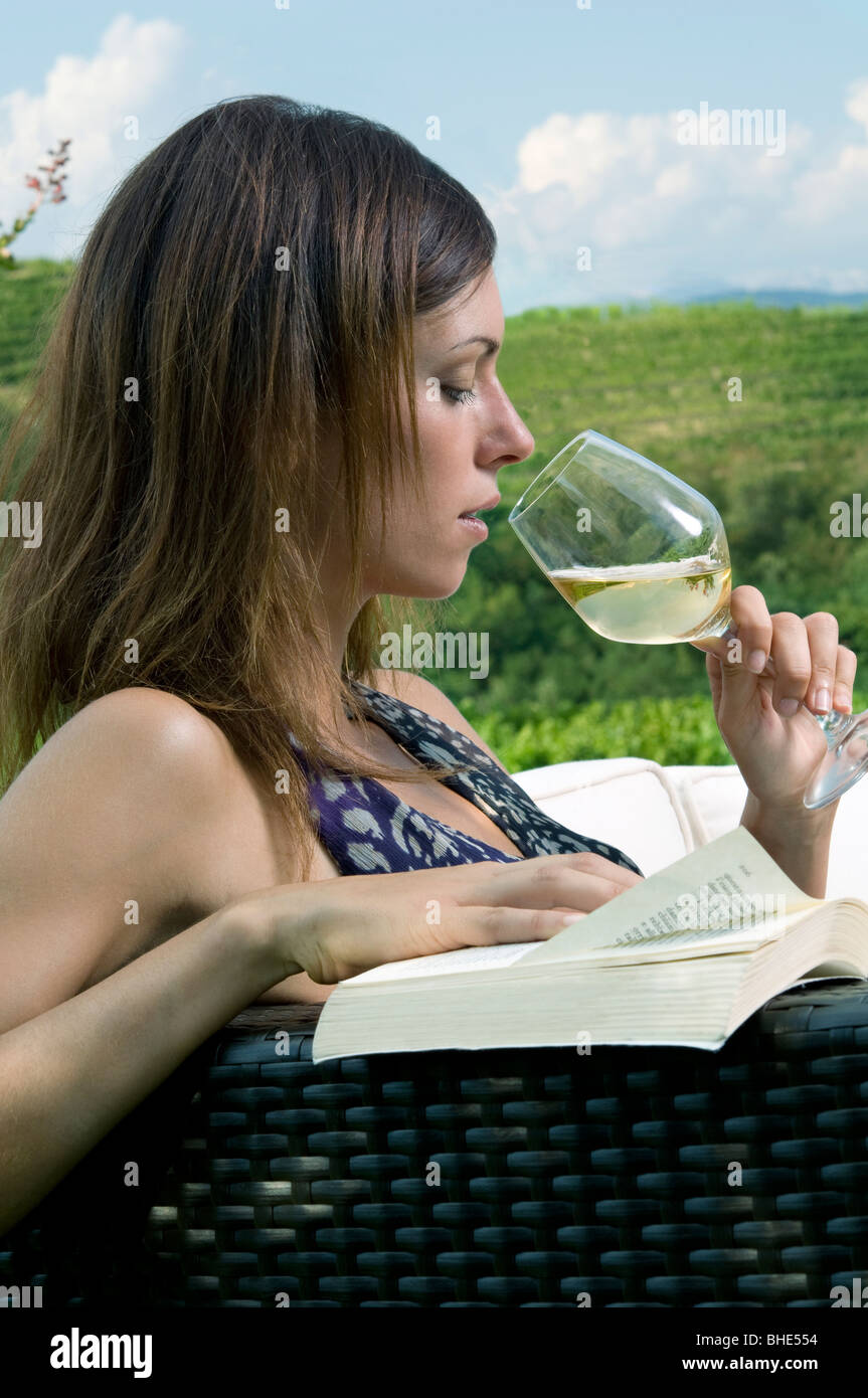 Young woman sitting on couch in vineyard drinking white wine and ...