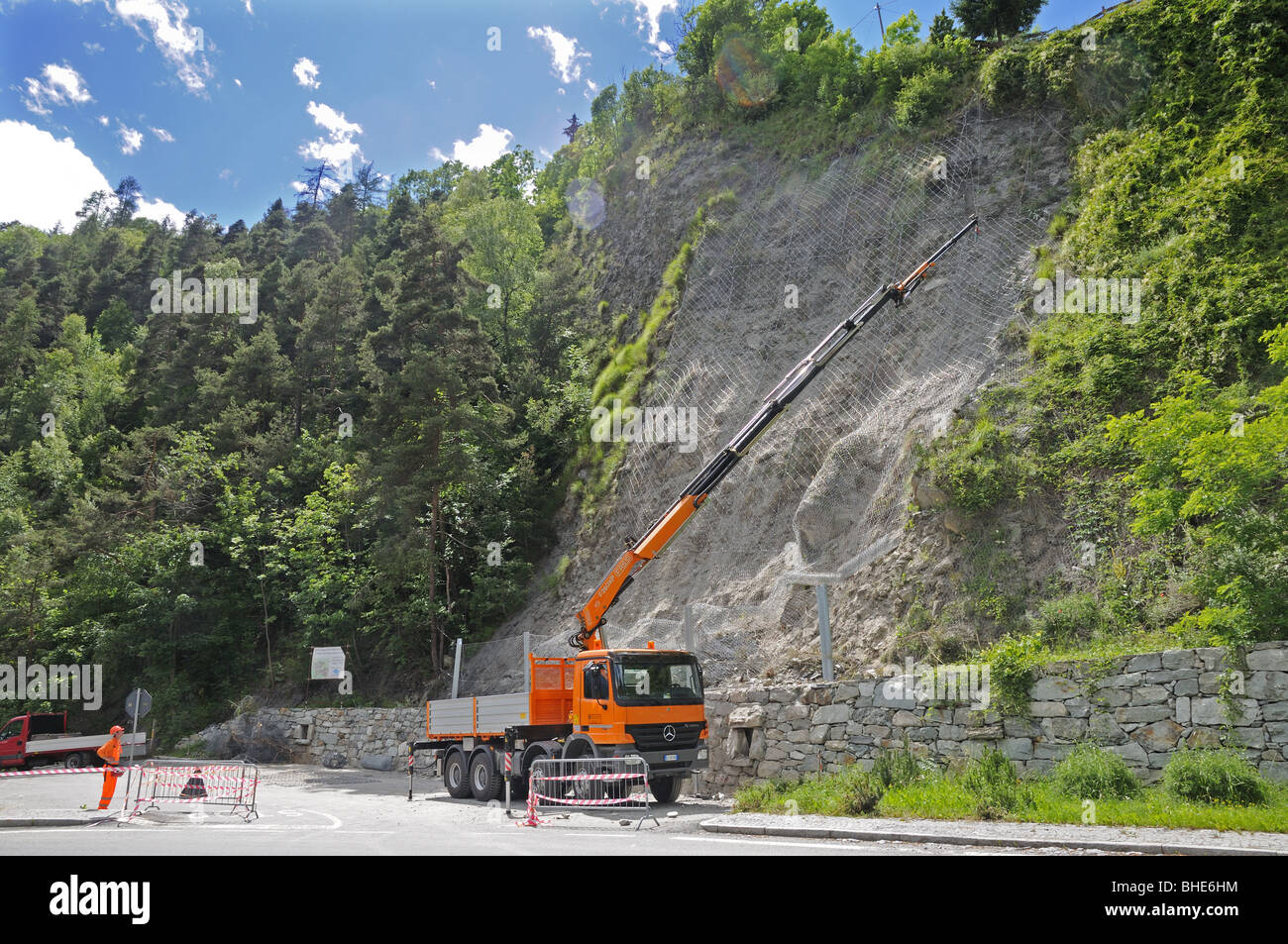 Man operating lorry with hydraulic crane to fix wire netting on hillside to overcome landslide Val Tournenche Italy Stock Photo