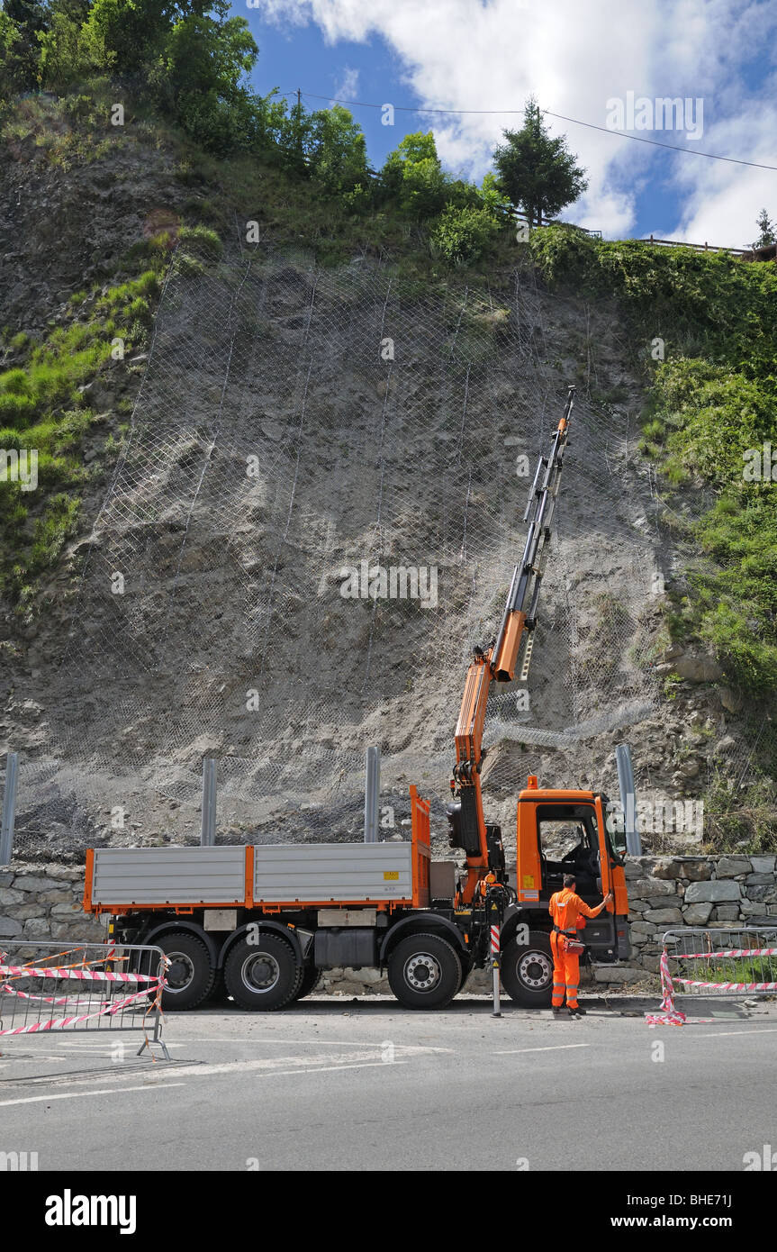 Man operating lorry with hydraulic crane to fix wire netting on hillside to overcome landslide Val Tournenche Italy Stock Photo