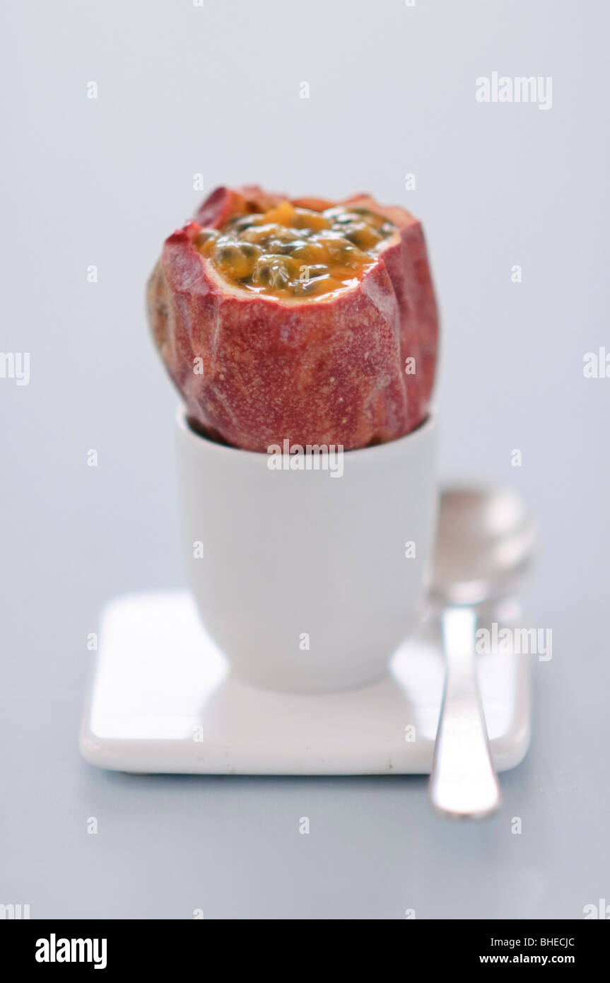 Passion fruit with top cut off sitting in an egg cup against blue background Stock Photo