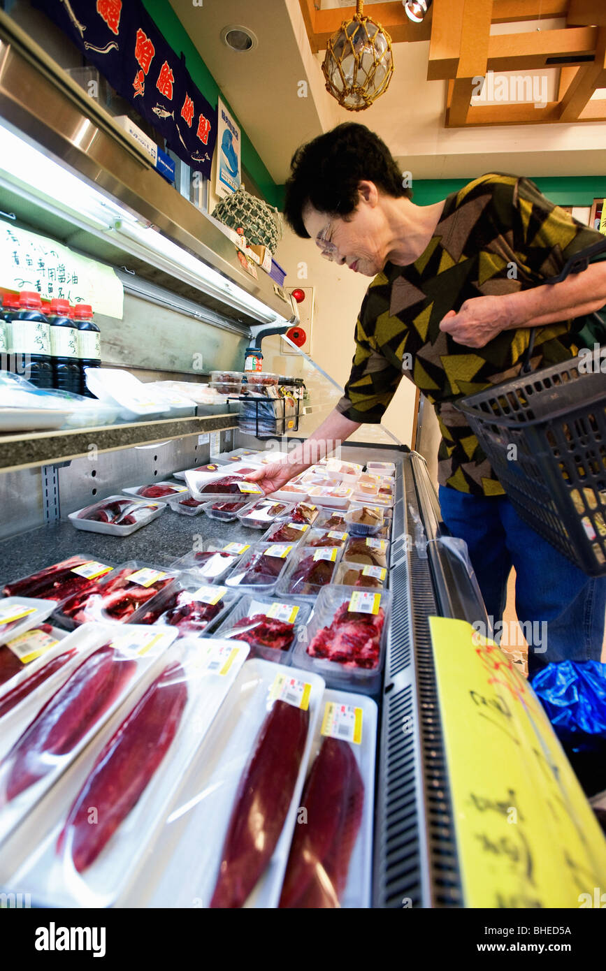 A woman looks at freshly caught and packaged dolphin meat and other sashimi products at a supermarket in Taiji, Japan Stock Photo