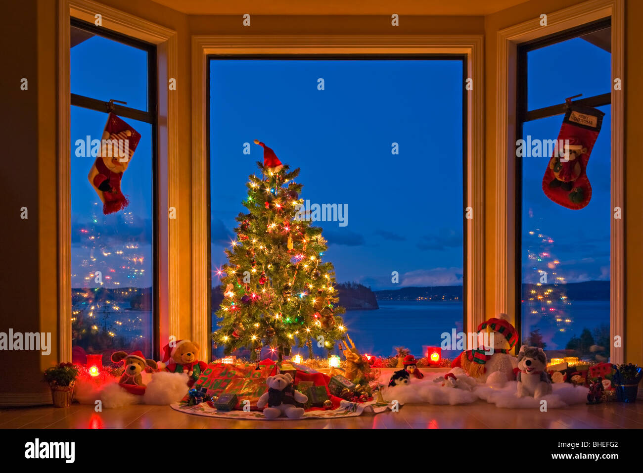 Christmas Tree with lights, decorations, and gifts in a window at dusk, The Artists Point, Hyde Creek, Port McNeill, BC, Canada Stock Photo
