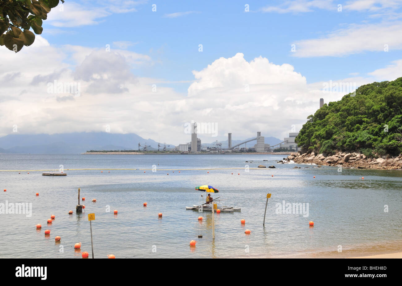 Lifeguard sitting on a floating platform, against a Lamma Power Station backdrop, Lo So Shing Beach, Lamma Island, Hong Kong Stock Photo