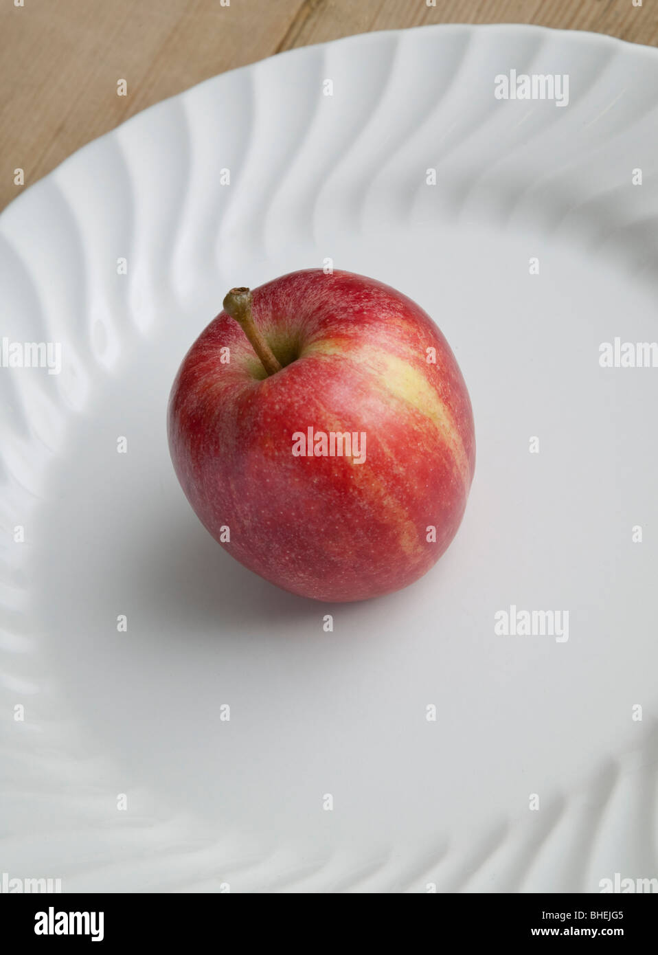 RED EATING APPLE ON WHITE PLATE ON WOODEN TABLE Stock Photo