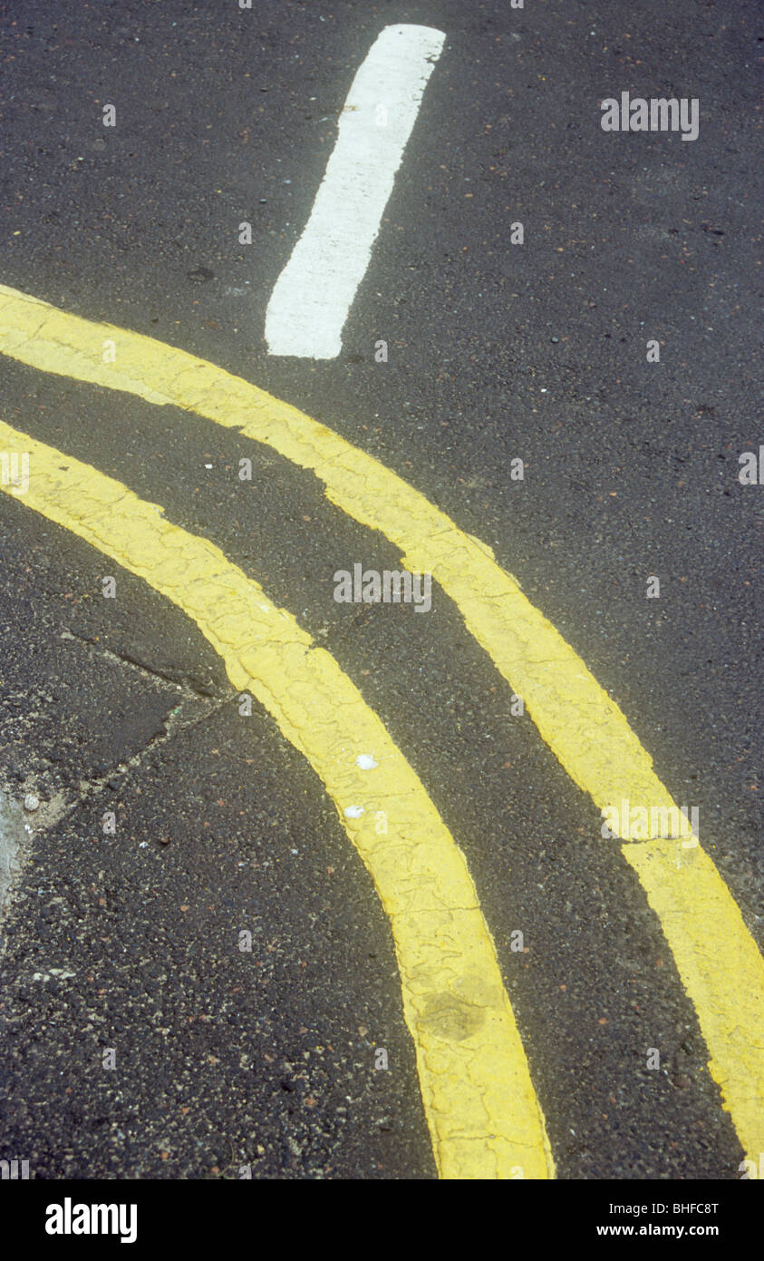 Detail of double yellow lines with blurred edges curving round corner or bend with single white line at right angles to them Stock Photo