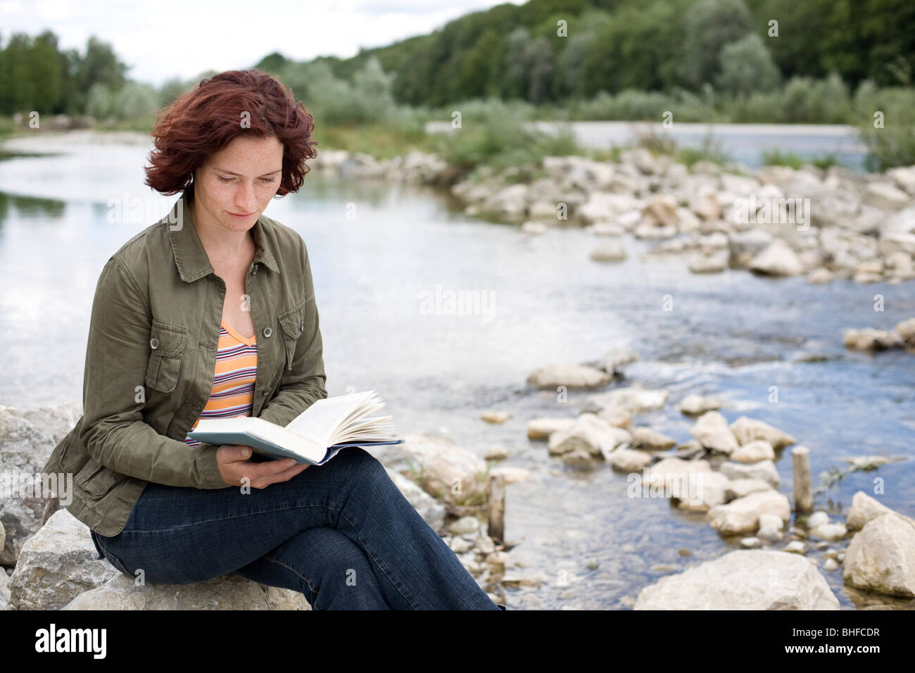 Mid adult woman reading a book at Isar riverbank, Munich, Bavaria ...