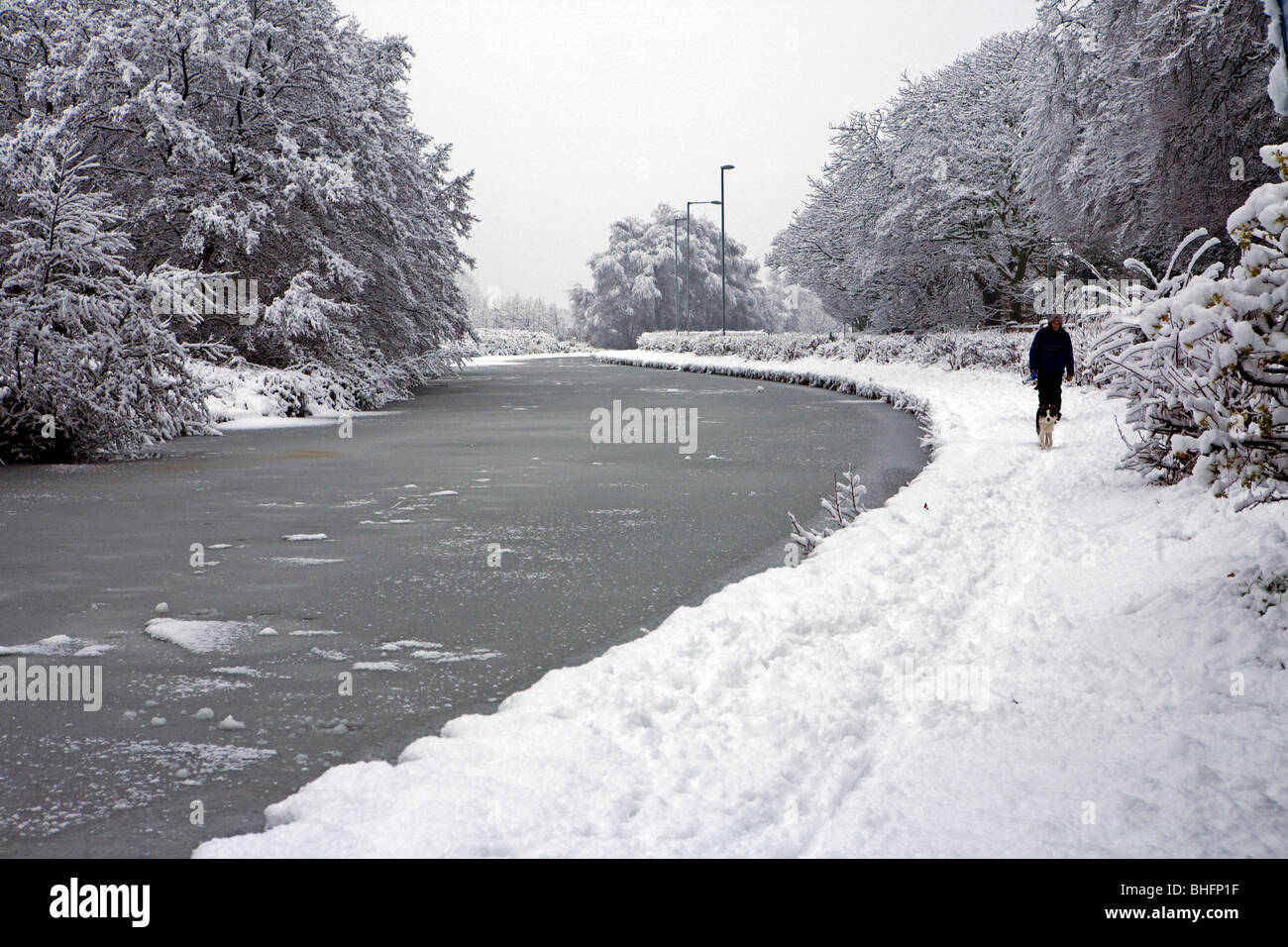 A man walks his dog through the snow along the side of a frozen Bridgewater Canal Stock Photo