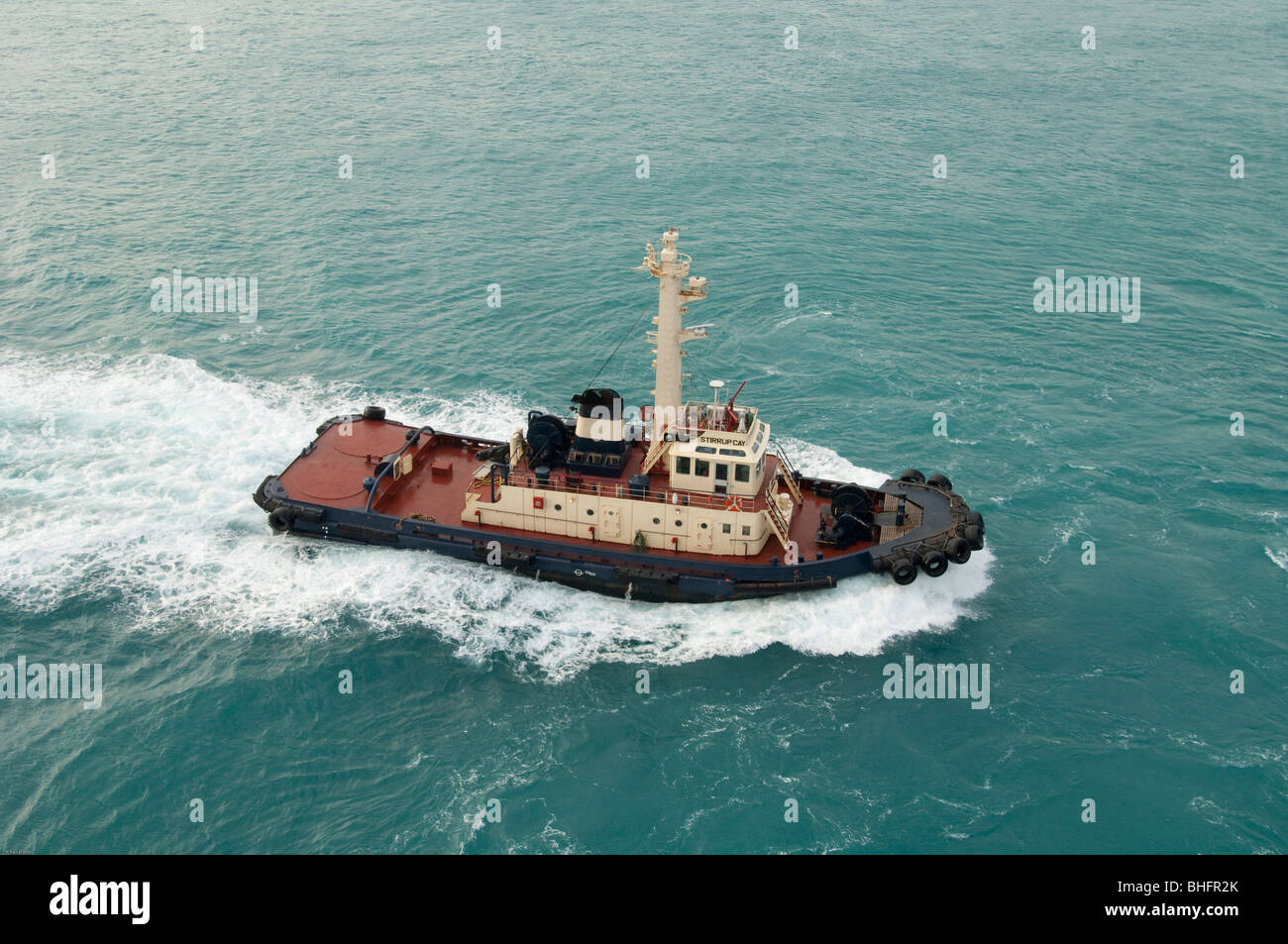 The tugboat 'Stirrup Cay' motors through through the water to provide harbor assistance to an ocean going cargo boat. Stock Photo
