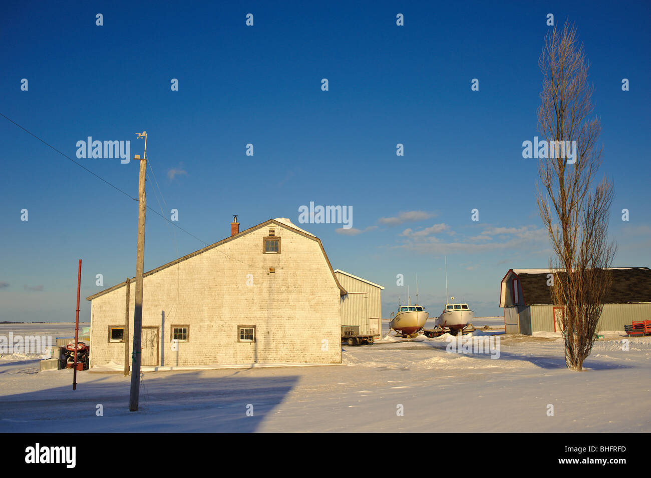 Fishing shack barn with lobster boats out of the water beside a frozen Miramichi Bay in New Brunswick Canada Stock Photo