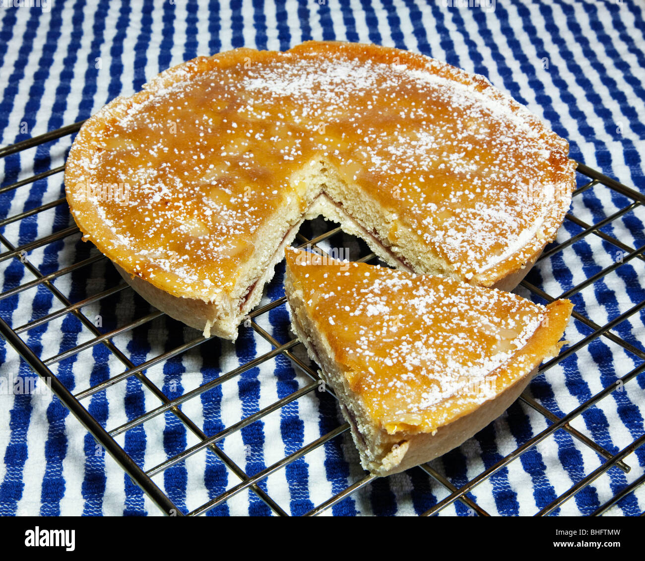 A bakewell tart with a slice cut out on a wire rack. Stock Photo