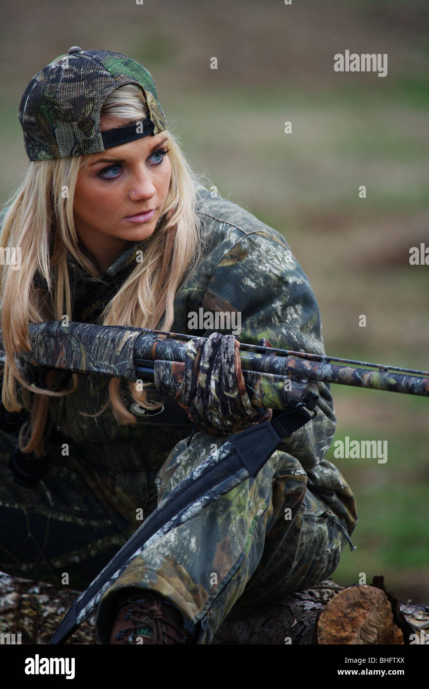 YOUNG WOMAN 21 Y.O. FEMALE  HUNTER SITTING IN HEAVY BRUSH GROUND BLIND WAITING FOR EVENING GAME TO APPEAR SHOTGUN CAMOFLAUGE Stock Photo