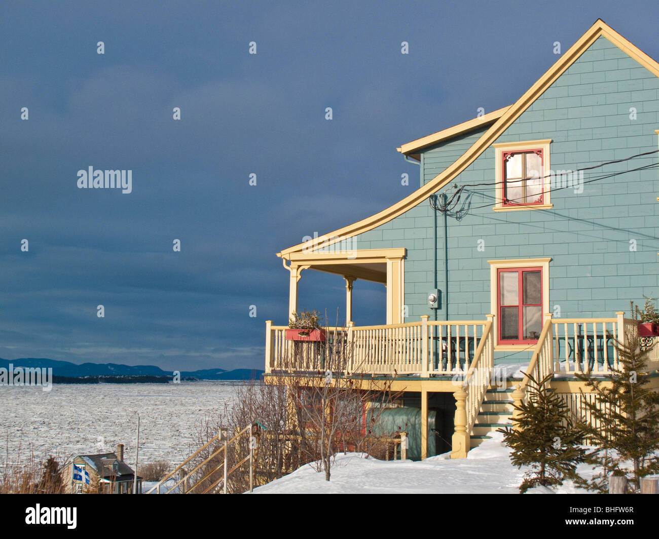 Blue house overlooking frozen st. lawrence river in quebec at sunset with dark sky Stock Photo