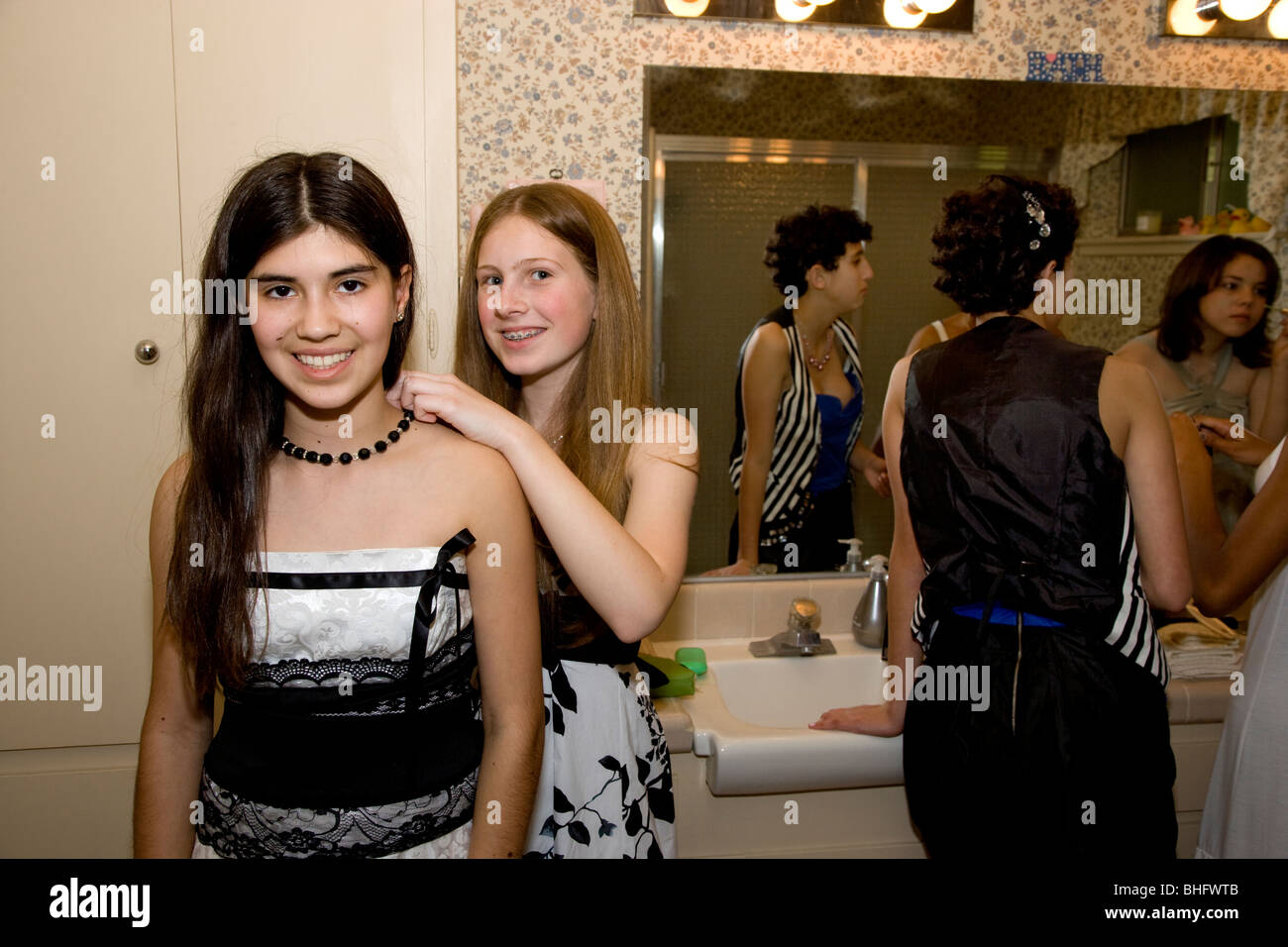 Preparing for their Formal Dance, five multi-ethnic girls putting on make up and doing their hair in the bathroom. Stock Photo