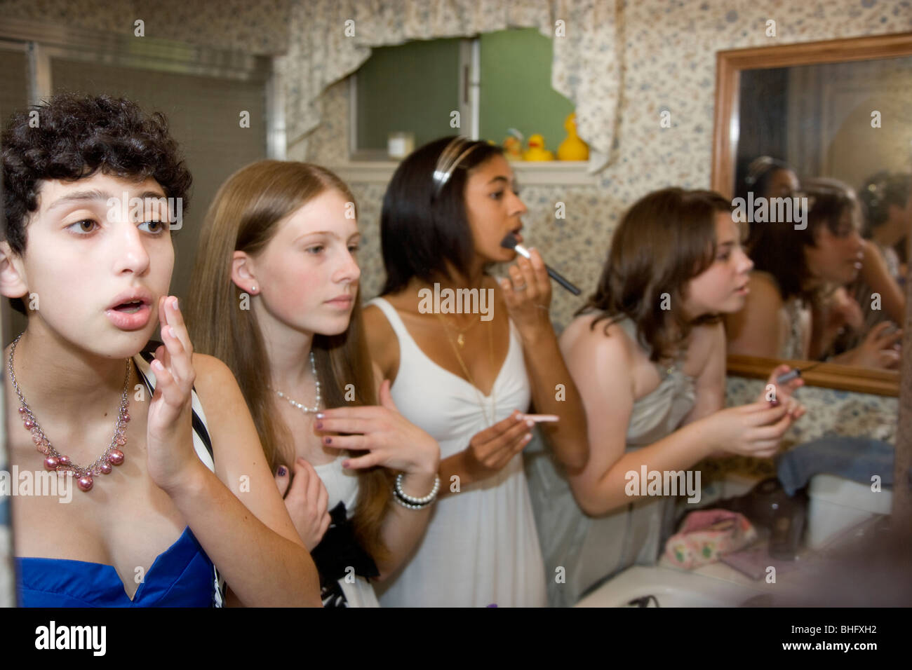Preparing for their Formal Dance, five multi-ethnic girls putting on make up and doing their hair in the bathroom. Stock Photo