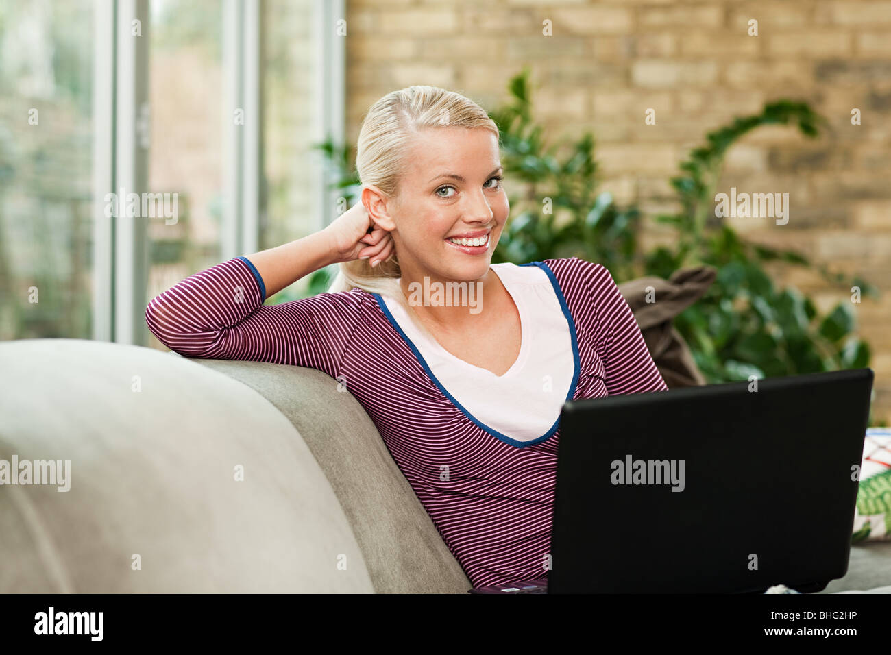 Young woman sitting on sofa with laptop Stock Photo - Alamy