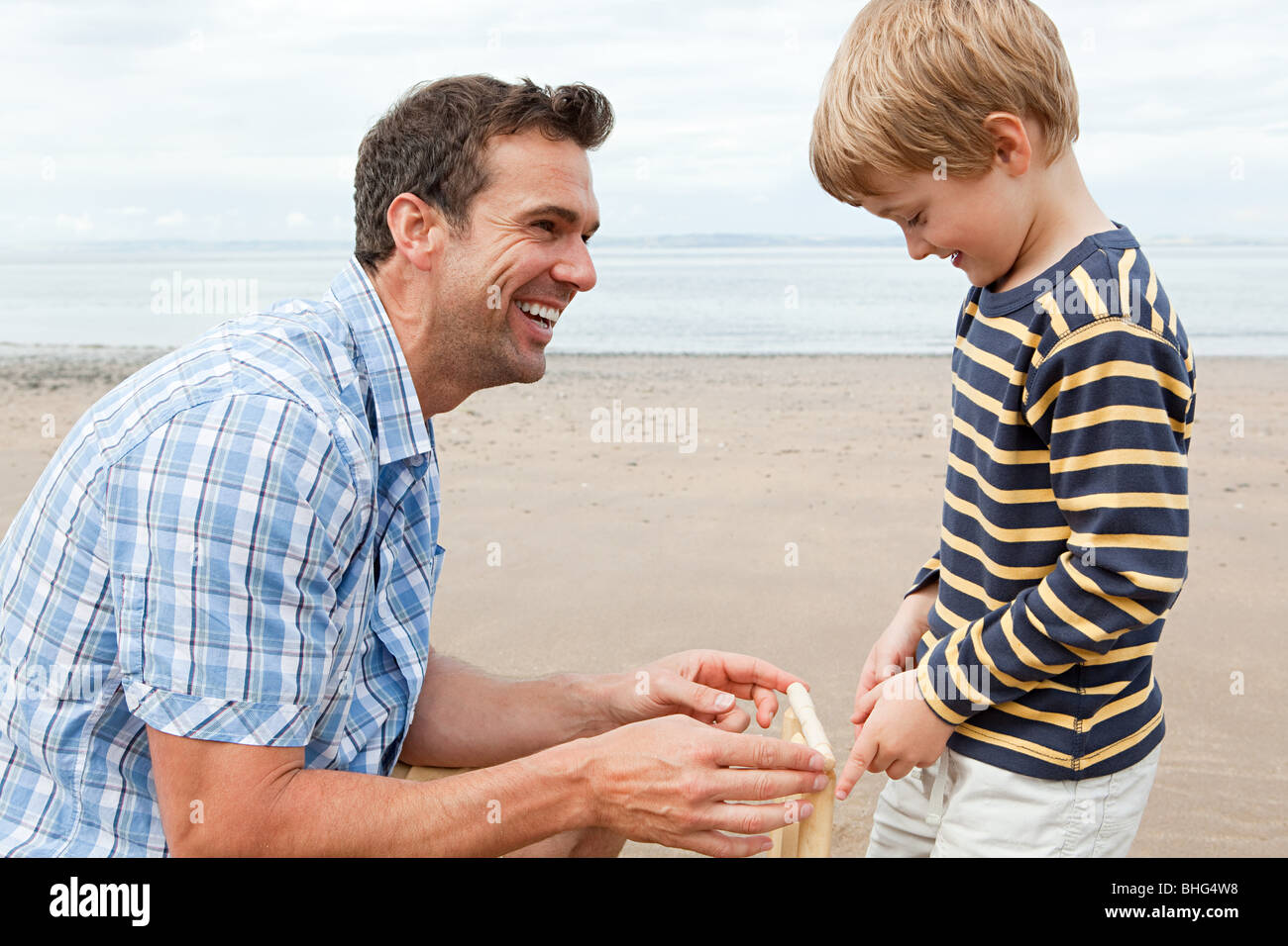 Father and son on beach with cricket stumps Stock Photo