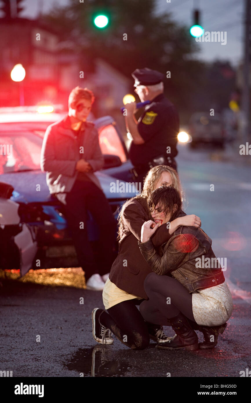 Young people and police officer at scene of car crash Stock Photo