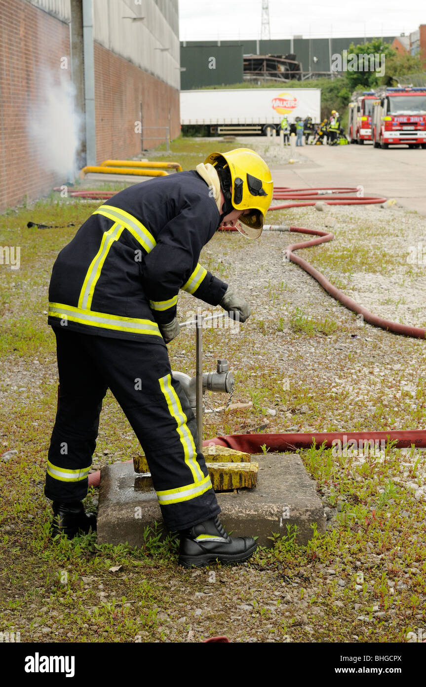 Fireman turns standpipe on at hydrant for water supply to fire Stock Photo