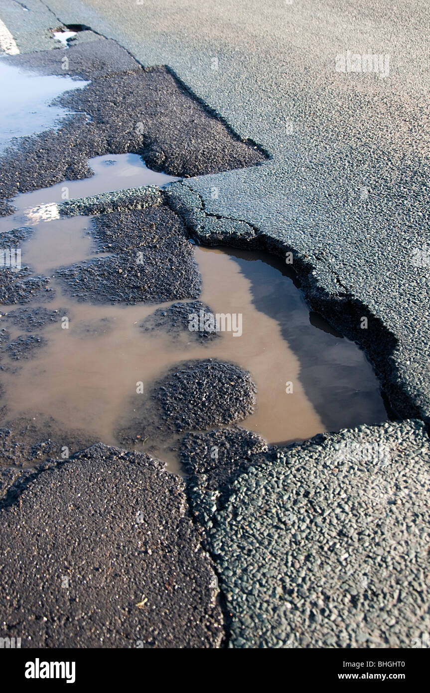 pothole potholes pot hole holes road roads with winter frost damage damaged rut ruts rutted ice heavy Stock Photo